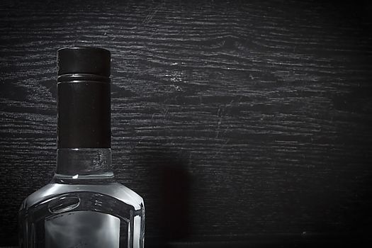 Neck of bottle with vodka on black wooden background