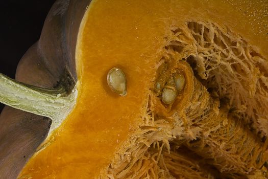 Cut ripe orange pumpkin close up on black background