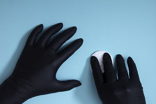 Hands in black nitrile gloves with a cotton sponge on a blue background