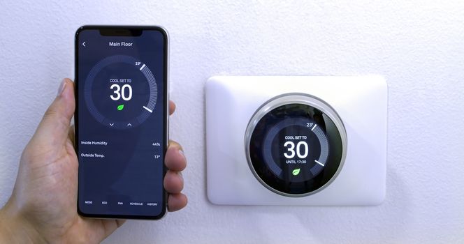 Calgary, Alberta, Canada. Aug. 29, 2020. A person saving energy with a iPhone 11 Pro Max using the nest app on celsius metrics using a wireless Nest Learning Thermostat on a white wall.