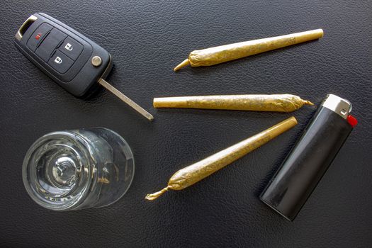 Cannabis Joints Cigarettes with car key, a shoot glass and a lighter on a leather black texture. Concept driving high. Drug-impaired driving is dangerous and against the law