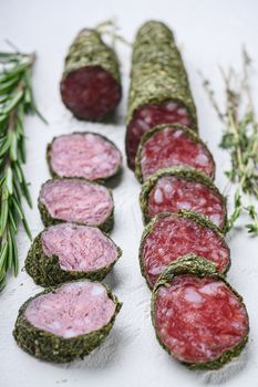 Variety of dry cured fuet and chorizosalami sausages, whole and sliced on white surface.