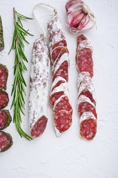 Variety of dry cured fuet and chorizosalami sausages, whole and sliced on white textured background.