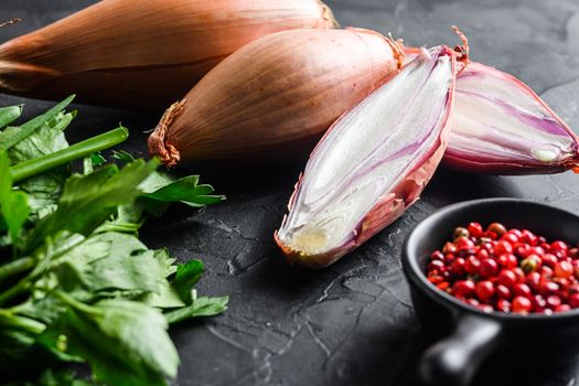 Organic shallot, eschalot or scallion raw ripe onions with greens and rose peppercorns sliced and halved black concrete textured background side view selective focus.