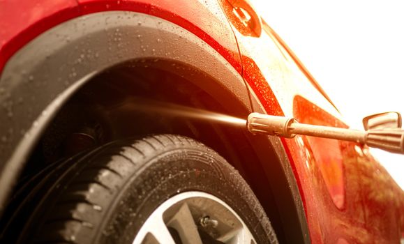 Close-up of man holding a high-pressure water sprayer for washing car rear wheel fender.