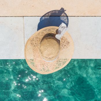 Graphic image of top down view of woman wearing big summer sun hat relaxing on pier by clear turquoise sea.