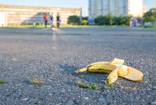 a discarded bitten banana lies on the road in the background of people leaving