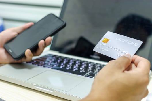 Man Shopping Online Using Laptop With Credit Card.Hands holding credit card and smartphone.