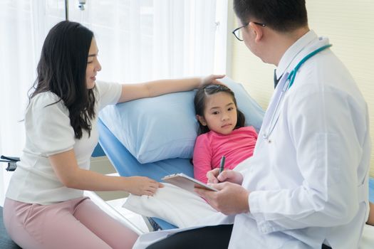 adult mother and preschool daughter consult pediatrician at the clinic. Young Asian male doctor examines physical health and asks for information from girls' parent