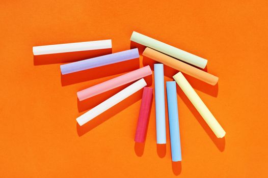 Multicolored thick sticks of chalk on orange background 