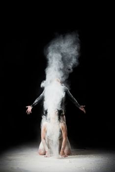 two beautiful young caucasian women in black bodysuits with a sports figure are dancing in a white cloud of flour on a black background, explosion and expresse in motion