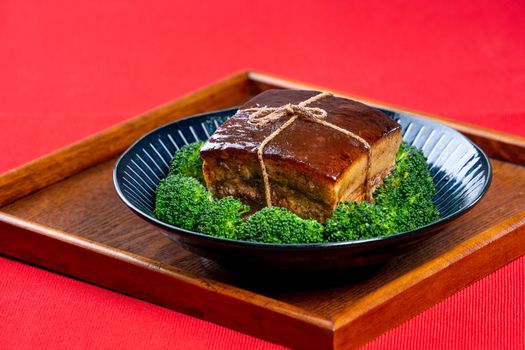 Dong Po Rou (Dongpo pork meat) in a beautiful blue plate with green broccoli vegetable, traditional festive food for Chinese new year cuisine meal, close up.