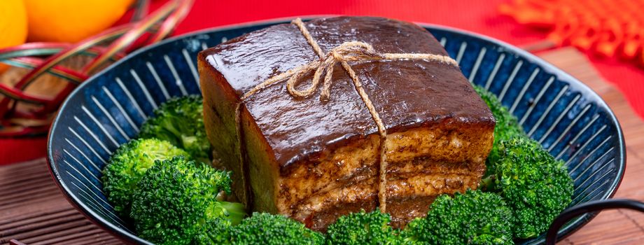 Dong Po Rou (Dongpo pork meat) in a beautiful blue plate with green broccoli vegetable, traditional festive food for Chinese new year cuisine meal, close up.