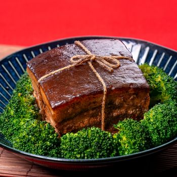 Dong Po Rou (Dongpo pork meat) in a beautiful blue plate with green broccoli vegetable, traditional festive food for Chinese new year cuisine meal, close up.