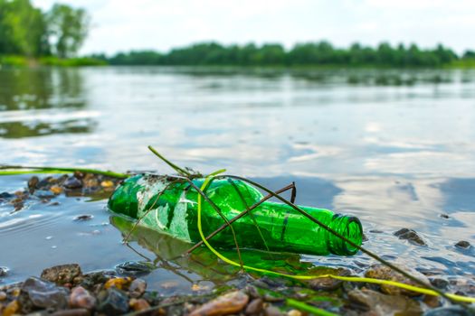 Glass bottle on the riverbank pollutes the environment. Nature pollution with garbage left by vacationers on the beach