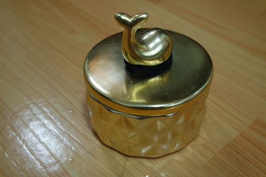 The decorative little golden pot with dolphin lid open, for room decoration. Golden pot on the vintage white background.