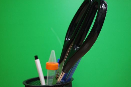 Closeup view of a stationery pot containing stationery items. stationery pot in front of a green background.
