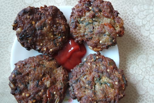 Delicious spicy fried round kebab served in white ceramic plate on a wooden floor with red sauce.