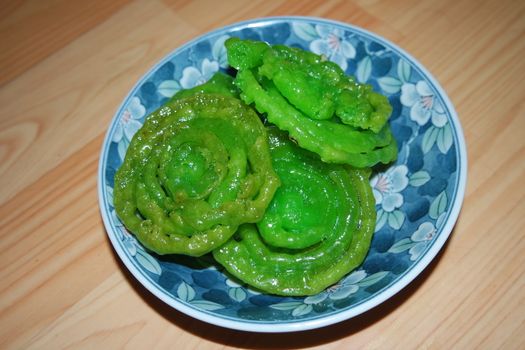 Crispy sweet Asian dessert green Jalebi cooked and served in ceramic plate, Indian sweet street food with juicy syrup, a closeup view.