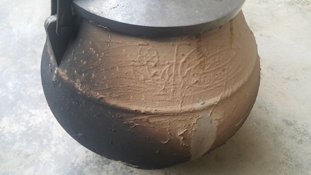 Pressure cooker covered with mud for cooking on fire. Cauldron type rural pressure cooker.