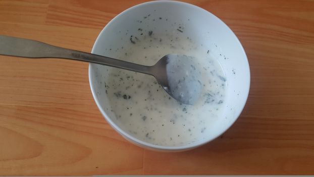 Close up of plain curd or yogurt or dahi in white ceramic bowl with silver spoon on a wooden surface. Curd is a dairy product obtained by coagulating milk in a process called curdling