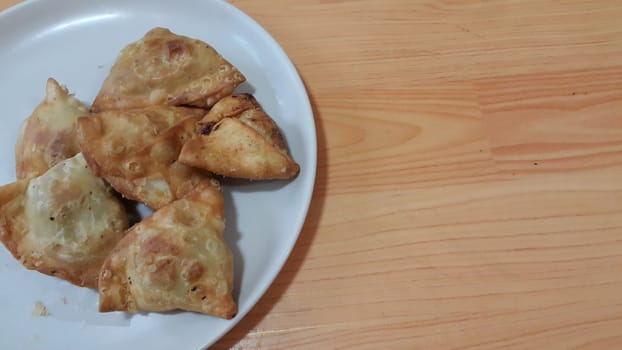 Closeup of delicious home made spicy and crunchy samosa pastries placed in a white ceramic plate on wooden floor