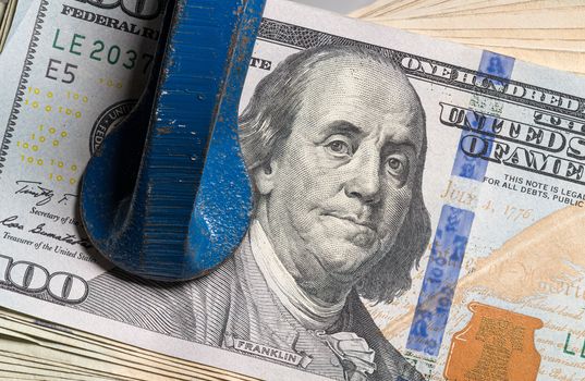 Concept for financial stress or recession. USA 100 dollar bills being squeezed between the jaws of a large vise or vice in detailed macro shot