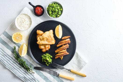 fish & chips with beer-battered cod and fries and a side of tartar sauce and mushy peas on rustic white stone table top view space for text side.
