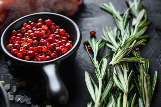 Rose Peppercorn and Rosemary herbs close up on black stone table with spices and raw meat near side view selective focus.