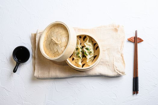 Bamboo steamer of Japanese gyoza, dumplings snack , with soy sauce and chopsticks served on white textured stone table top view.