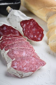 Spanish salcichon slices with panini and herbs on white textured background.