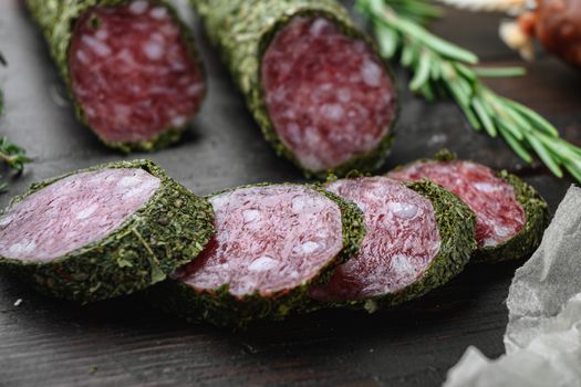 Variety of dry cured chorizo, fuet and other sausages cut in slices with herbs on dark wooden background.