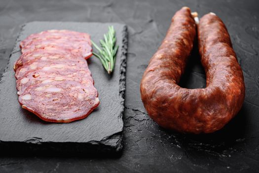 Whole and sliced chorizo sausage on black background.