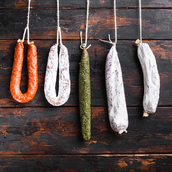 Spanish dry sausages hang from a rack at market on old wooden table, square format.