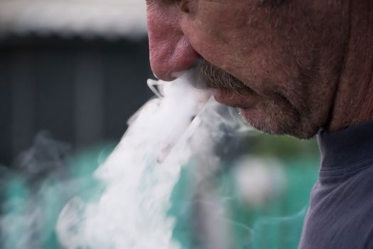 A man with a mustache smokes a cigarette in close-up. Thick smoke from tobacco Smoking and the concept of health. Nicotine addiction in humans.