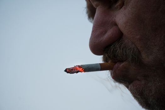 A man with a mustache smokes a cigarette in close-up. Thick smoke from tobacco Smoking and the concept of health. Nicotine addiction in humans.