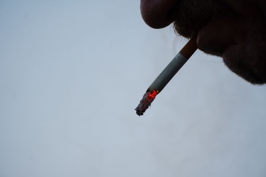 A man with a mustache smokes a cigarette in close-up. Thick smoke from tobacco Smoking and the concept of health. Nicotine addiction in humans.