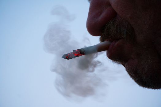 A man with a mustache smokes a cigarette in close-up. Thick smoke from tobacco Smoking and the concept of health. Nicotine addiction in humans.