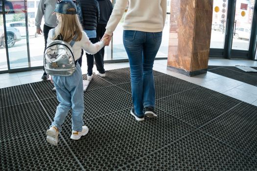 The mother leads the child by the hand with a backpack in the lobby of a shopping center, airport or train station go to the exit door. A girl with a baby girl.