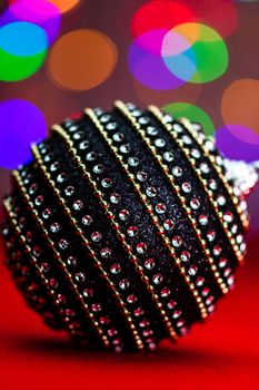 Black and shiny Christmas ball bauble in a Christmas composition on blurred lights background.