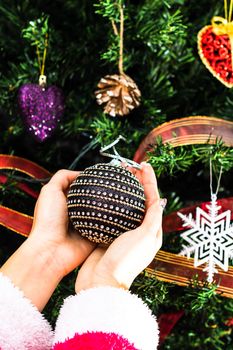 Hands holding Christmas ornament in front of Christmas tree. Decorating fir branches with Christmas decorations.