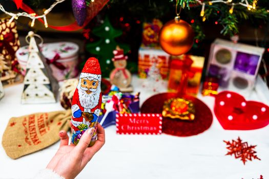 Hand holding Santa Claus chocolate figurine in front of the Christmas tree. Decorating Christmass tree isolated