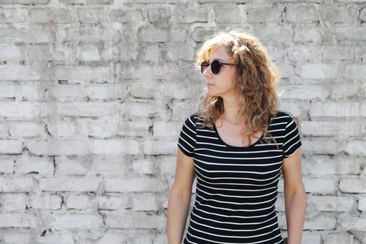 Woman portrait in sunglasses, free space for inscription. White brick wall in the background