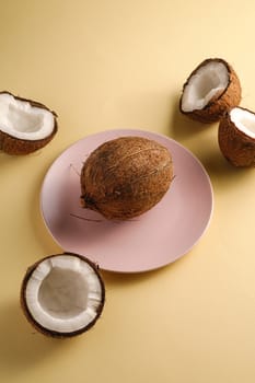 Coconut in pink plate with nut fruits on cream yellow plain background, abstract food tropical concept, angle view