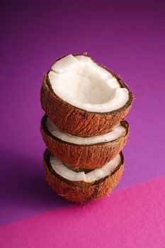 Stacked coconut fruits on violet and purple plain background, abstract food tropical concept, angle view