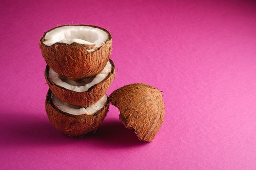 Stacked coconut fruits on pink purple plain background, abstract food tropical concept, angle view copy space