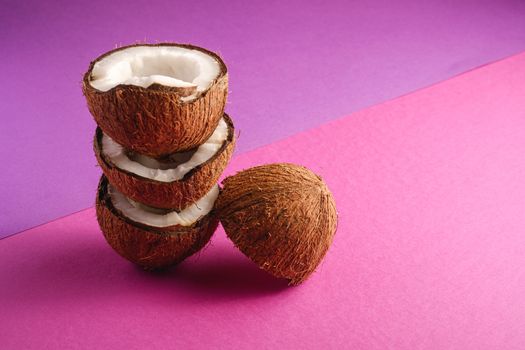 Stacked coconut fruits on violet and purple plain background, abstract food tropical concept, angle view copy space