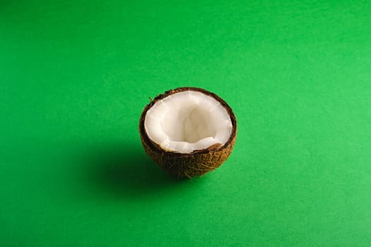 Single coconut fruit on green plain background, abstract food tropical concept, angle view copy space