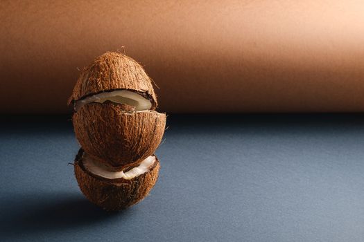 Stacked coconut fruits on brown and blue grey folded paper background, abstract food tropical concept, angle view copy space