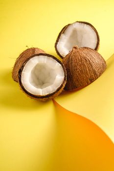 Coconut fruits on folded paper yellow plain background, abstract food tropical concept, angle view